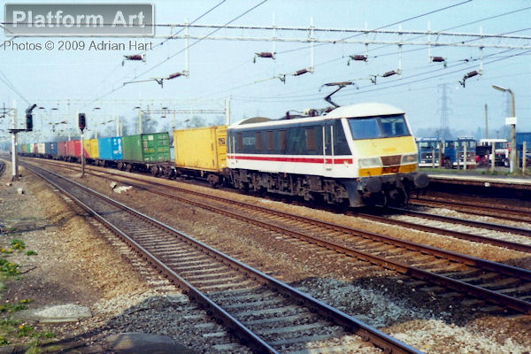 Class 90 90005 Financial Times provides the motive power for the 4E75 07.26 Garston - Felixstowe South freightliner, seen passing Rugeley Trent Valley on 31st March 1990.
